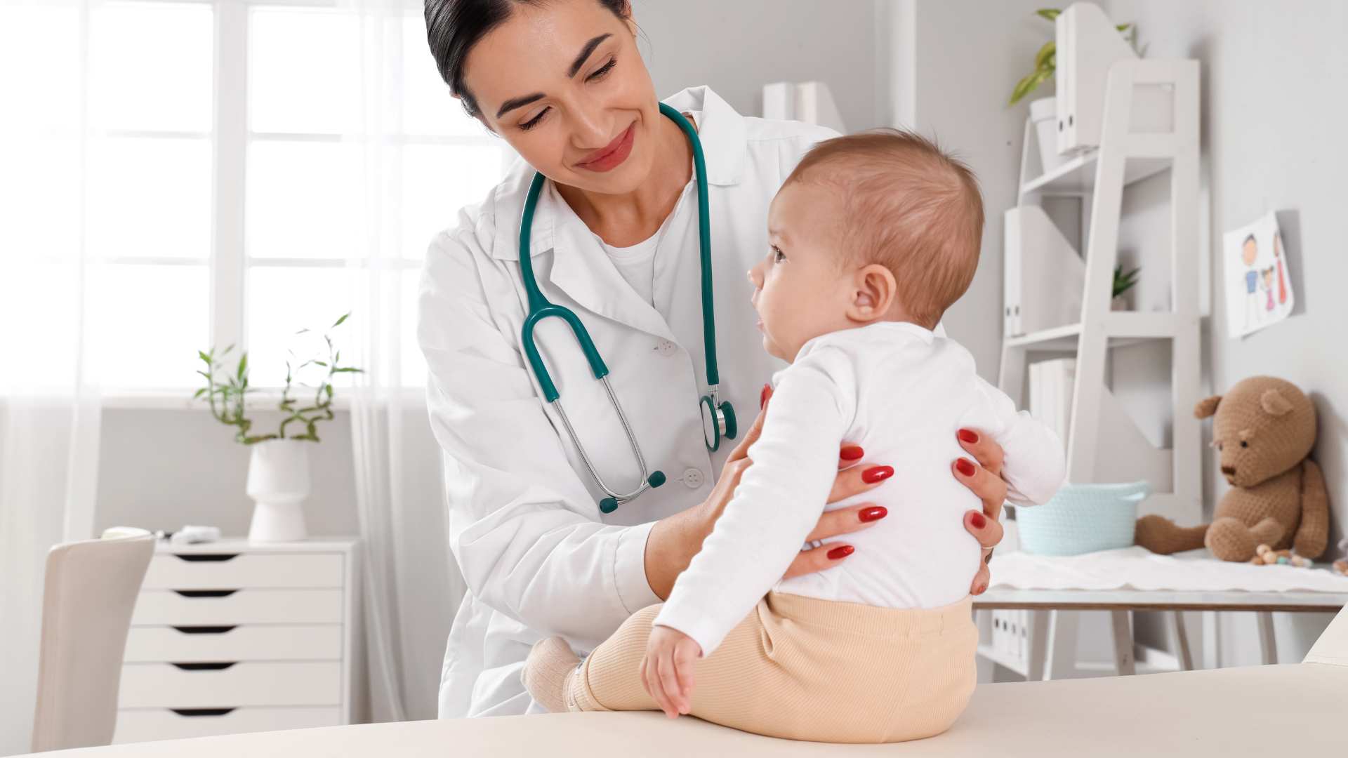 A baby sitting on an exam table with a doctor nearby, illustrating a routine visit about 12‑month‑old developmental milestones