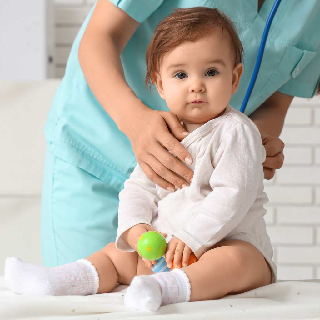 A female pediatrician in teal scrubs gently examines a baby