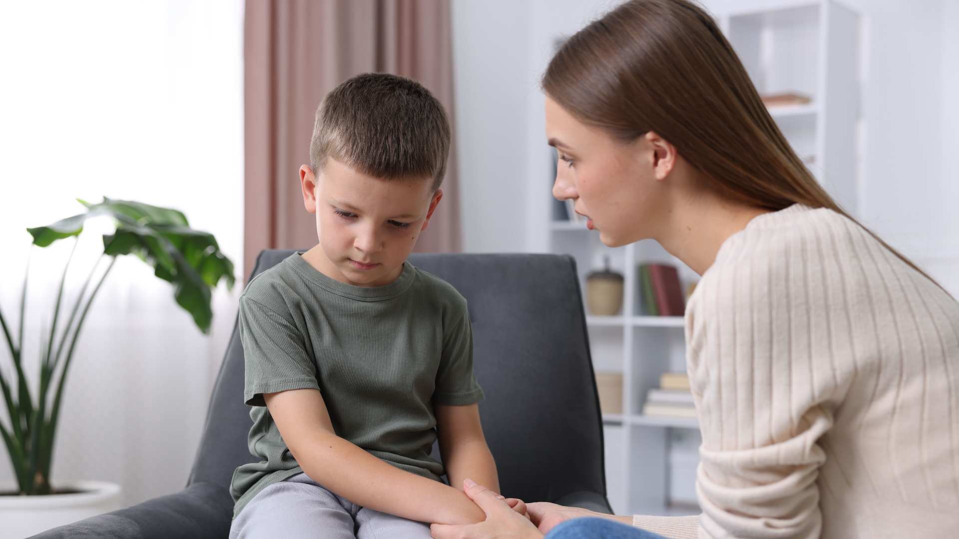 A mother gently holding her son’s hands while he looks down, showing concern about his eye contact