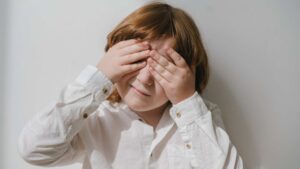 A young kid with hands over their eyes, used to illustrate autism and eye contact