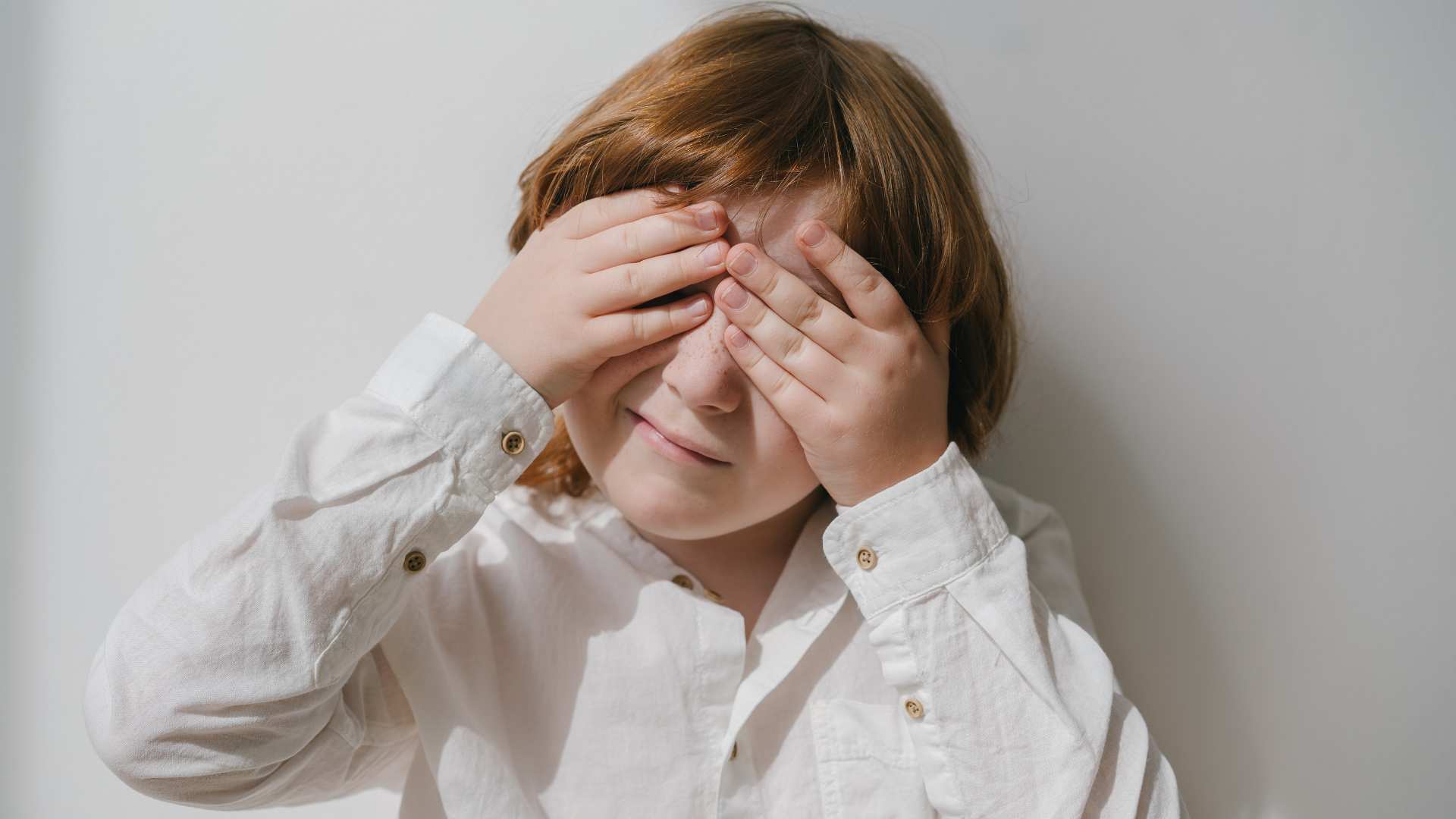 A young kid with hands over their eyes, used to illustrate autism and eye contact