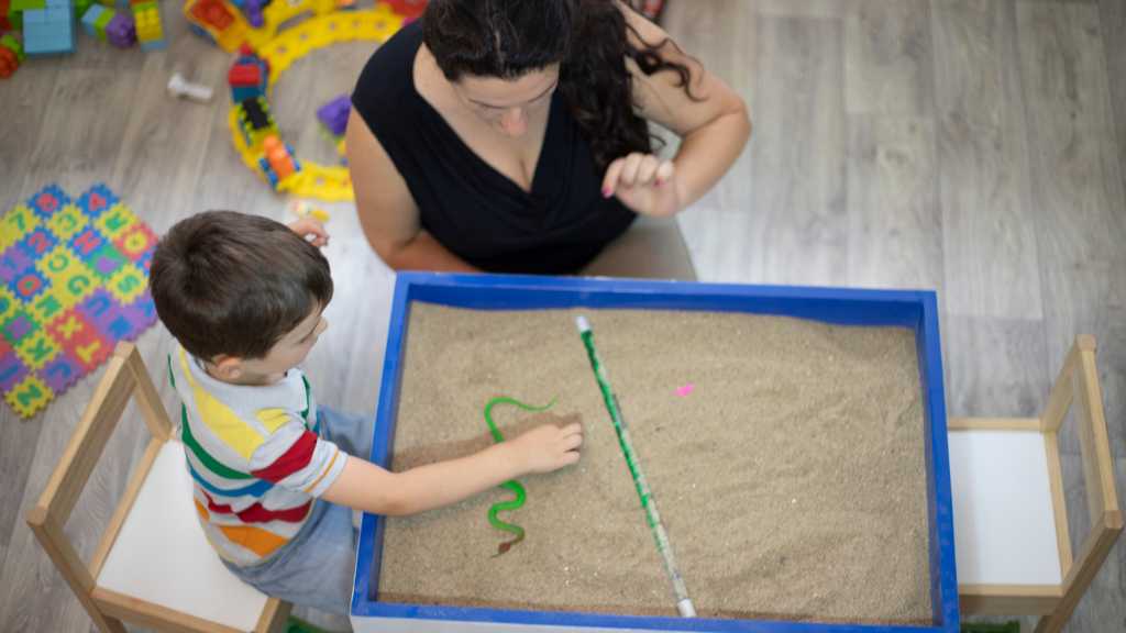 Therapist guiding child with sand tray activity, representing ABA therapy and early intervention for every level of autism