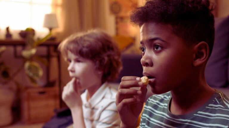 Two children watching a screen intently while eating snacks, illustrating how characters like Sonic the Hedgehog can support special interests in autism and help children with ASD engage and learn.