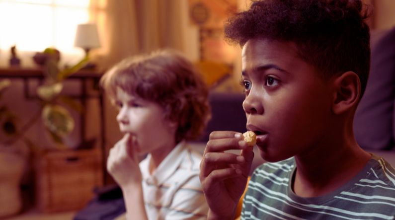 Two children watching a screen intently while eating snacks, illustrating how characters like Sonic the Hedgehog can support special interests in autism and help children with ASD engage and learn.