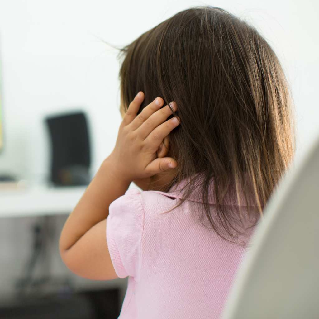 Child seen from behind covering ears while a cartoon plays on a screen