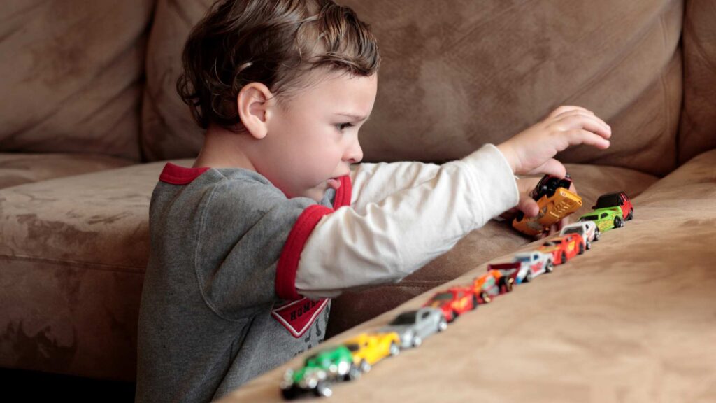 Child sitting on a couch carefully lining up small toy cars in a row