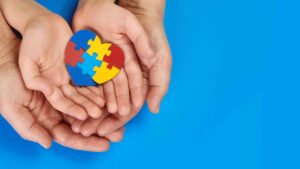 Multiple hands clasping the autism awareness logo, in this picture a puzzle piece in the shape of a heart, for World Autism Awareness Day.