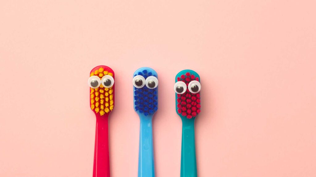 Three differently colored toothbrushes with googly-eyes to signify dental care for autism.