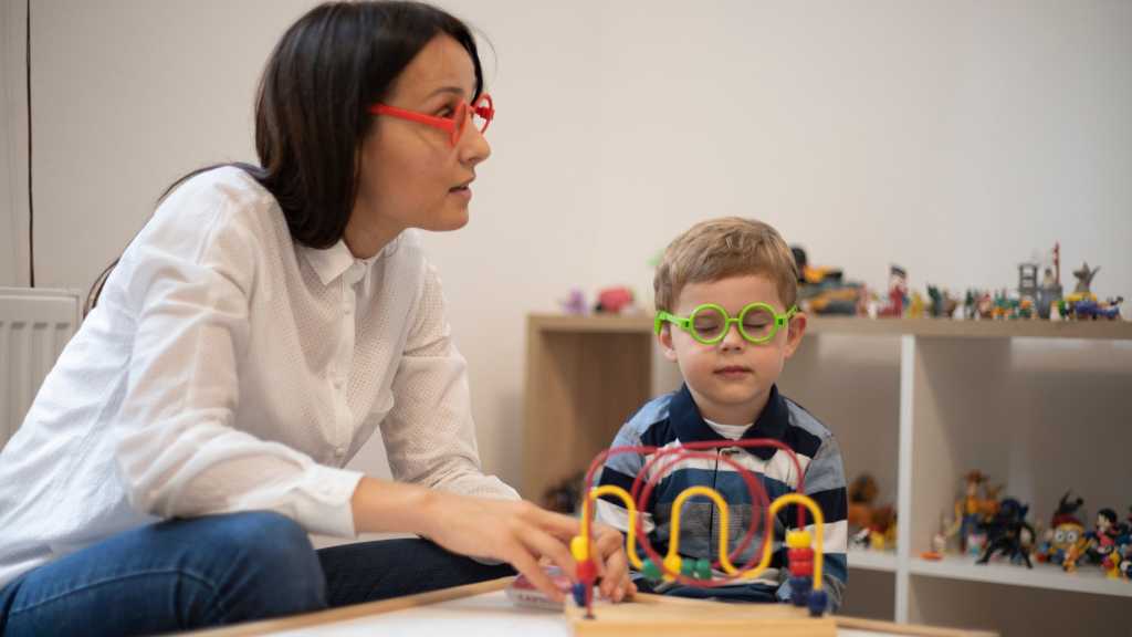 Una mujer y un niño participan en una terapia de juego en una habitación llena de juguetes.