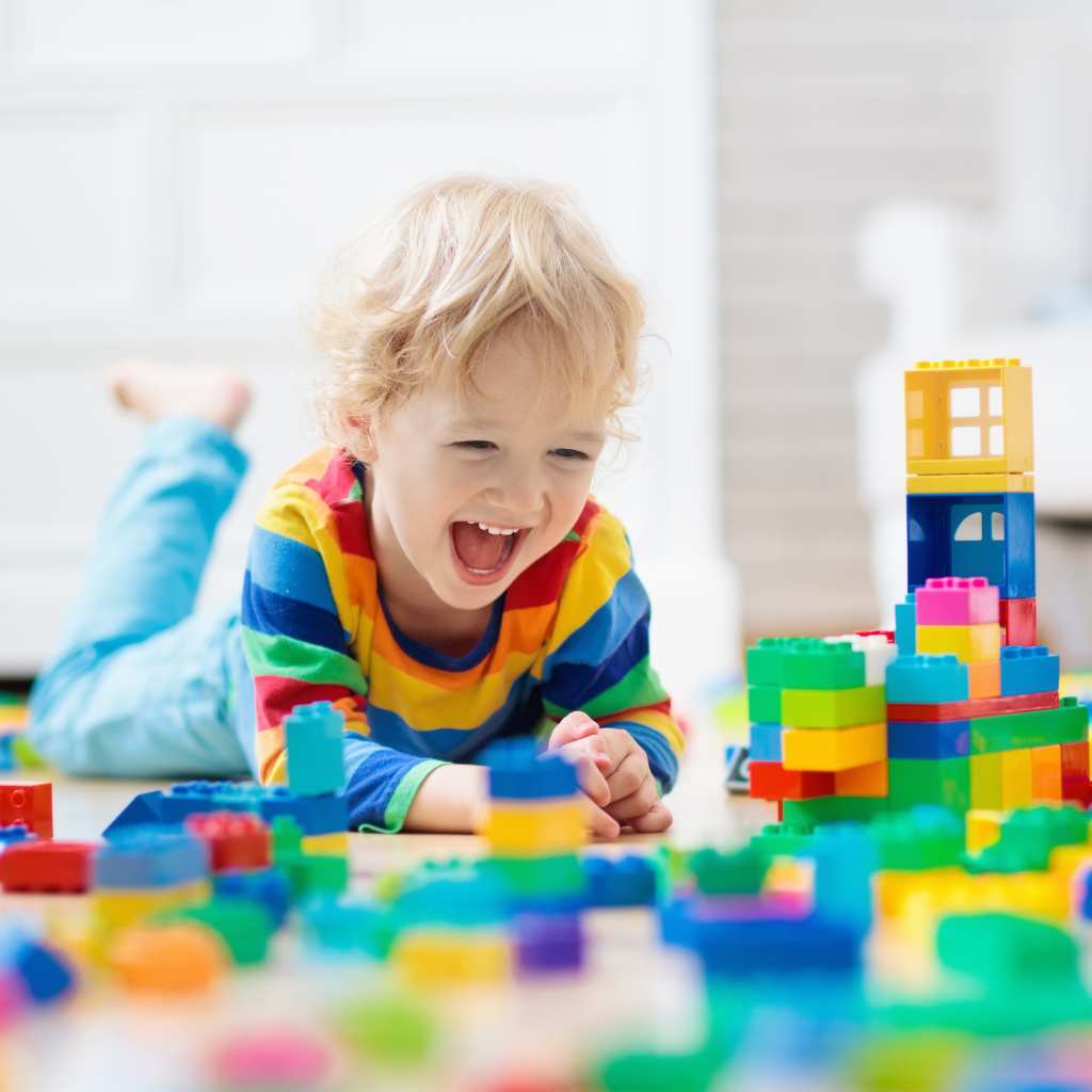 Happy child in a colorful striped shirt playing with building blocks on the floor, enjoying independent play