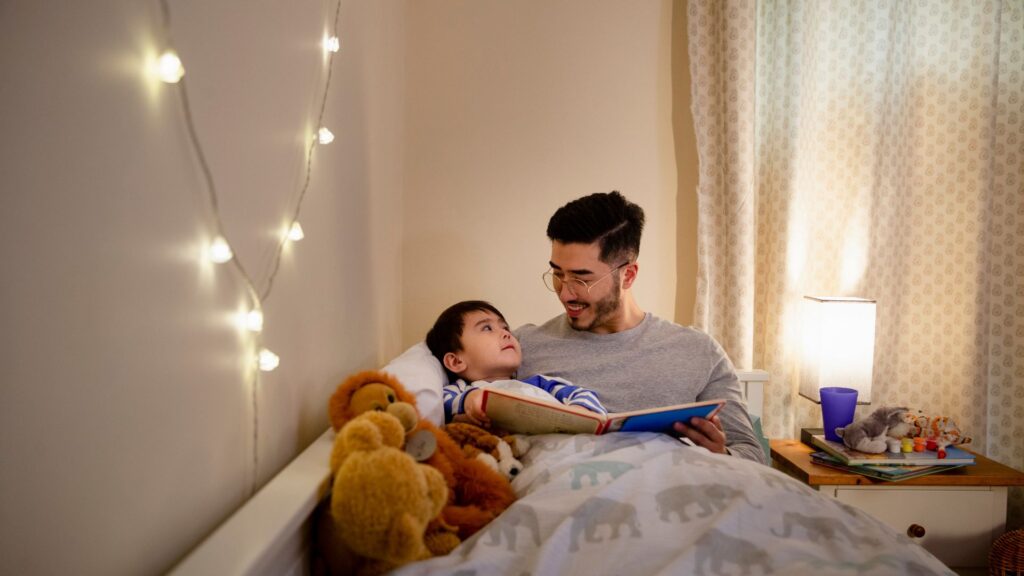 Importancia de las Rutinas para el Autismo. Un padre le lee un cuento antes de dormir a su hijo.