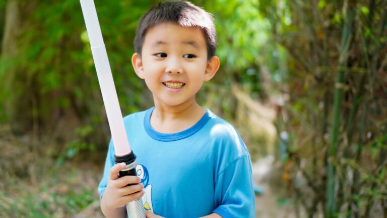 Young boy plays with toy light saber for May the 4th, looks extremely happy