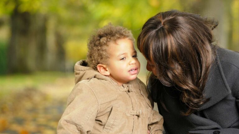 Adult leaning toward a toddler outdoors as the child looks away, relating to My Toddler Doesn't Respond to Their Name