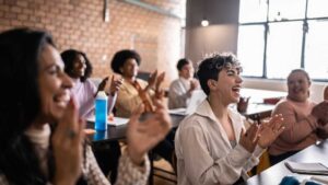 Group of diverse people smiling and clapping in a classroom setting, symbolizing the meaning of neurodiverse vs neurodivergent and celebrating human difference