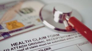 A stethoscope resting on a health claim form with U.S. currency in the background, symbolizing healthcare costs, open enrollment decisions, and ABA insurance coverage for families seeking autism therapy.