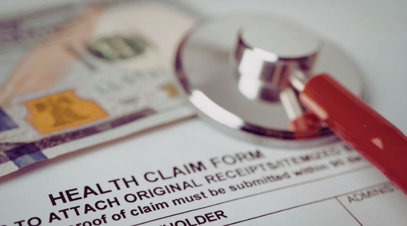 A stethoscope resting on a health claim form with U.S. currency in the background, symbolizing healthcare costs, open enrollment decisions, and ABA insurance coverage for families seeking autism therapy.