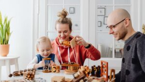 Parents and their toddler daughter smile while playing together with wooden developmental toys at a table, illustrating the role of parents in ABA therapy