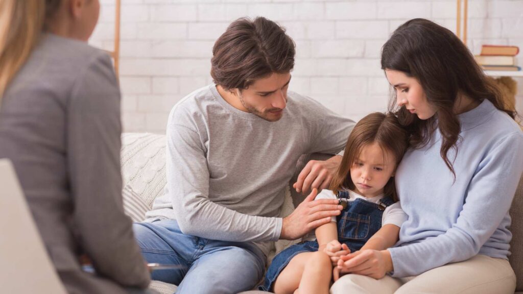 Parents comfort their young daughter during a therapist consultation, illustrating that grief after a child's autism diagnosis