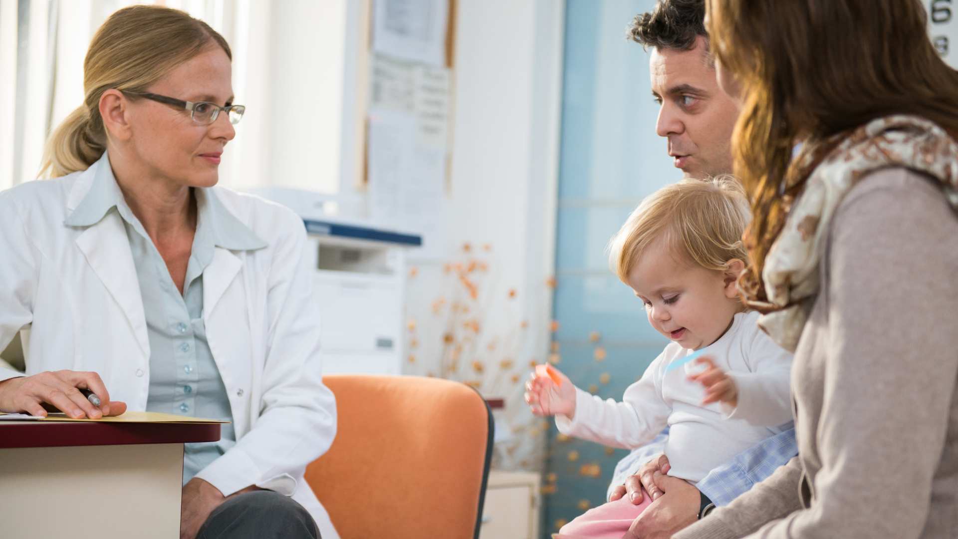 Parents hold their toddler while asking questions to a pediatrician during their first developmental screening appointment