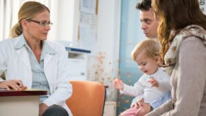 Parents hold their toddler while discussing autism concerns with a pediatrician in a clinic office