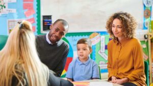 Parents meet with their child's teacher in a classroom advocating for your child with autism in school, with their young son seated between them
