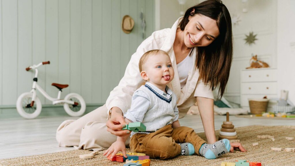 Photo of a caregiver playing with a young child on the floor and wondering Is my 18-month-old behind