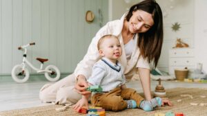 Photo of a caregiver playing with a young child on the floor and wondering Is my 18-month-old behind