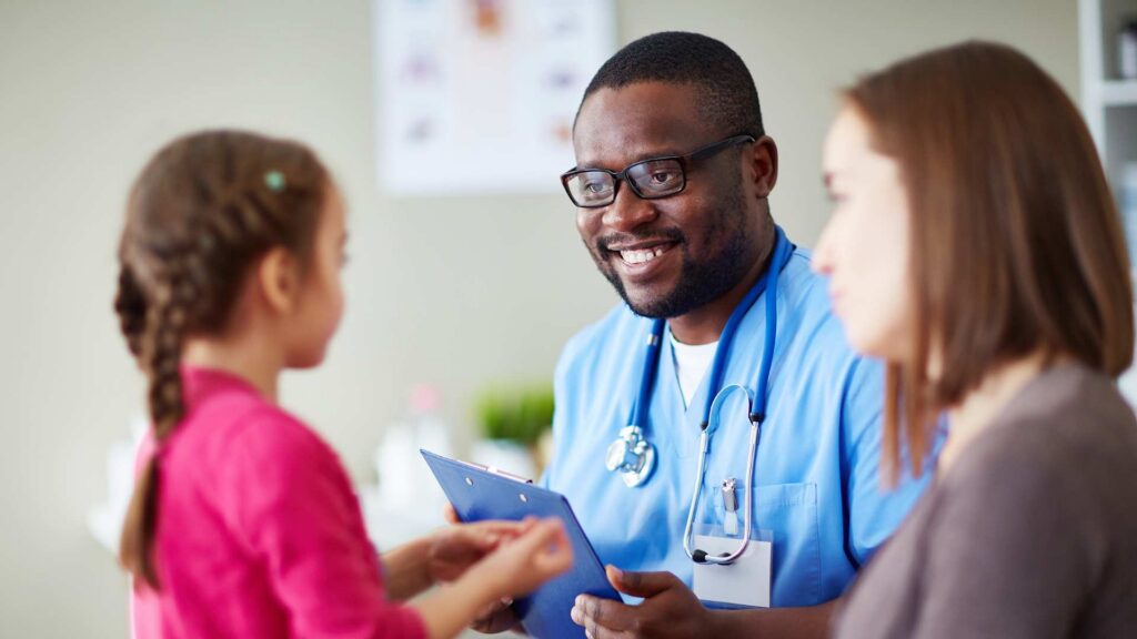 Smiling clinician holds an autism evaluation report on a clipboard while speaking with a mother and her young daughter in a clinic