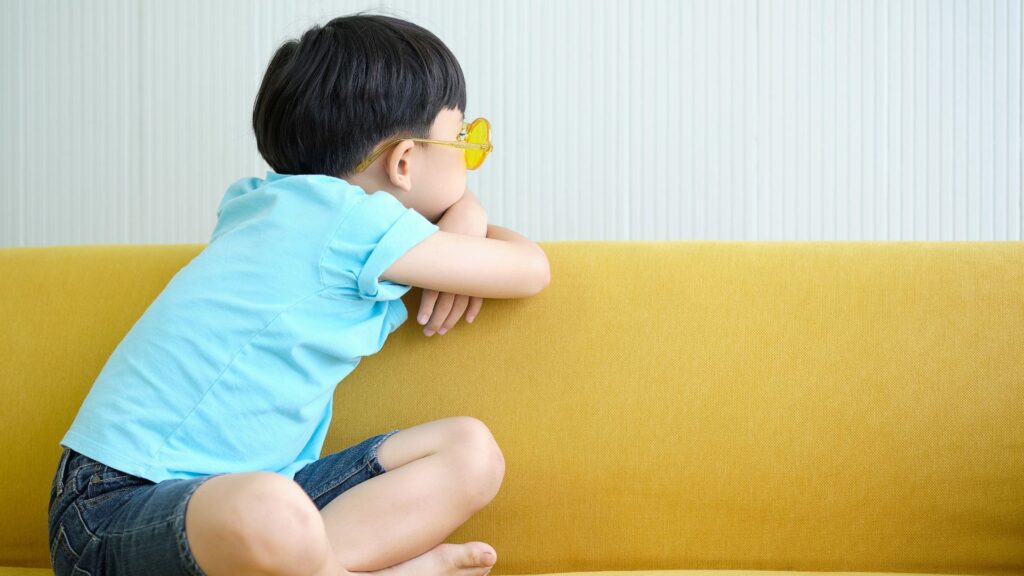 Qué causa el autismo. Imagen de un niño reflexionando mientras se apoya en el respaldo de un sofá