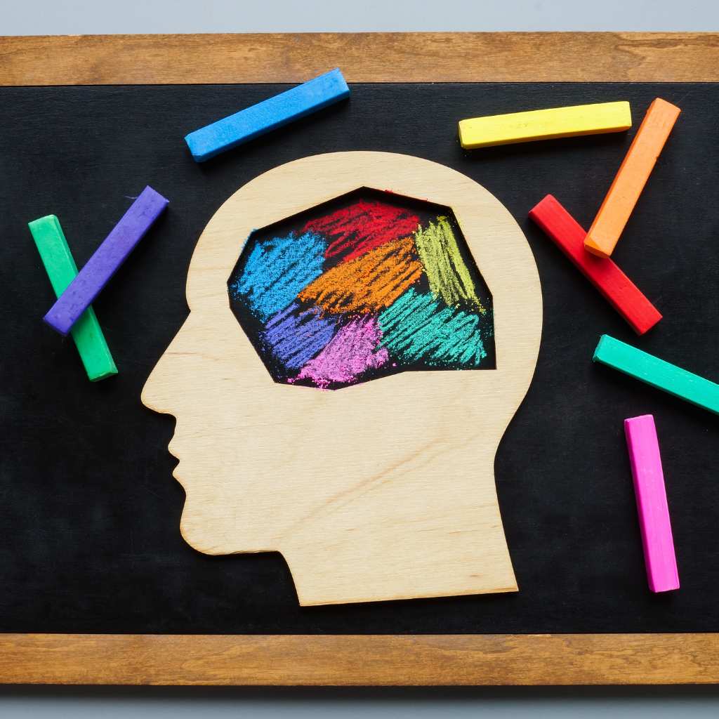 Wooden head cutout with colorful chalk strokes inside the brain on a blackboard, representing neurodivergence