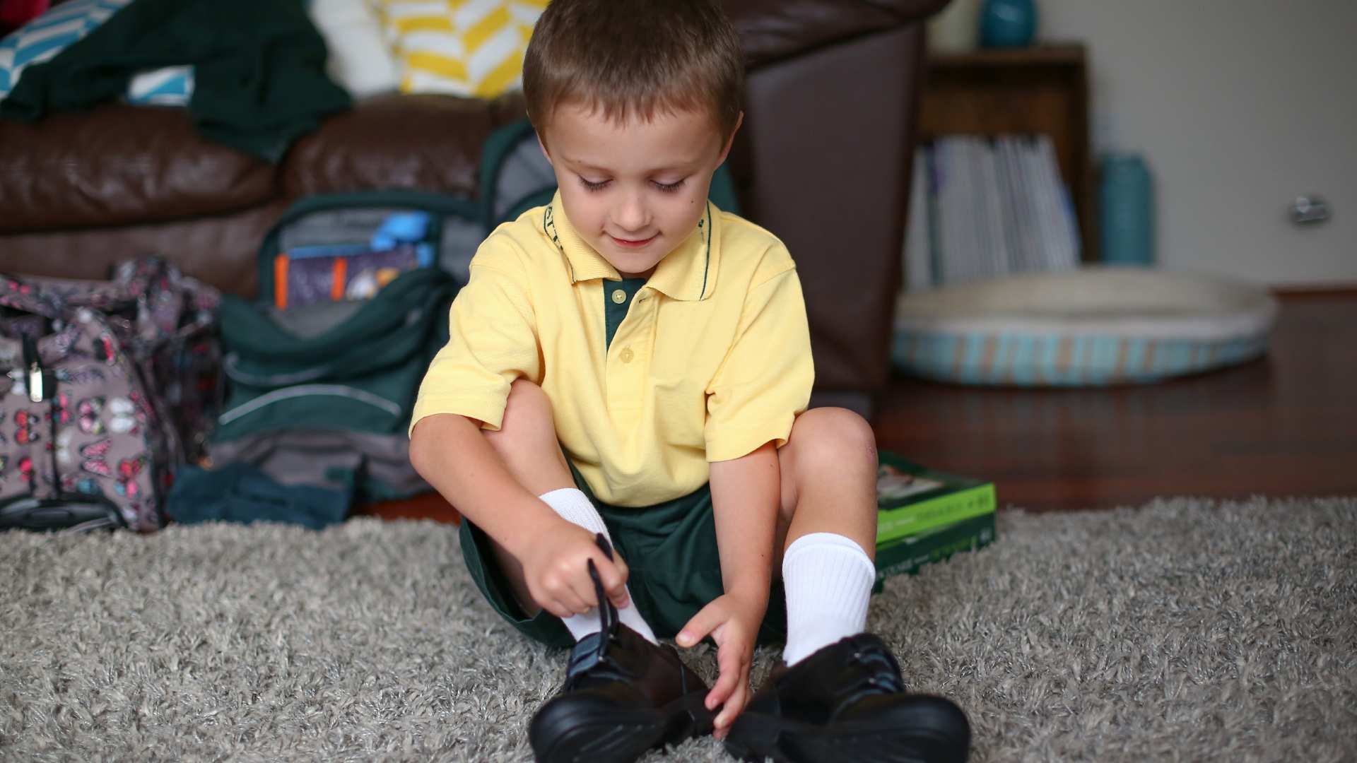 Young boy sits on the floor putting on his socks and shoes as he gets ready for school, demonstrating school readiness and independence skills
