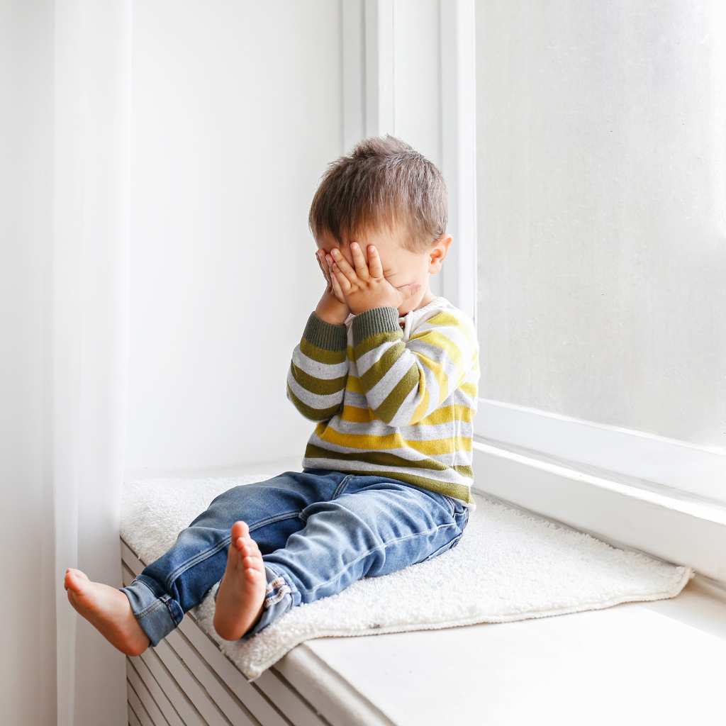 Young child sitting on a windowsill avoiding eye contact