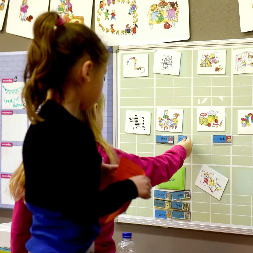 Young girl selecting a picture card from a visual schedule board in a classroom, using school accommodations for structured learning